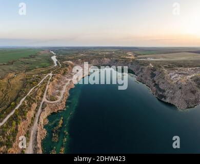 Alte geflutete Steinbruch mit großen Steinen am Abend warmes helles Licht mit kleinen trockenen Pflanzen in der malerischen Ukraine bedeckt. Luftpanoramik dro Stockfoto