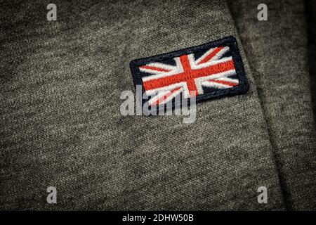 Extreme Nahaufnahme eines Bekleidungslabels mit der britischen Flagge (Union Jack Flag) auf einem grauen Stoff genäht. Made in Kingdom, Konzept. Stockfoto