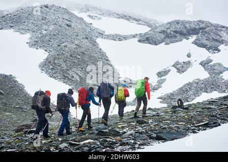 Rückansicht von männlichen Wanderern mit Rucksäcken, die auf felsigen Pfaden in Winterbergen wandern. Gruppe von Bergsteigern mit Trekkingstöcken, die den felsigen Hügel erklimmen. Konzept von Reisen, Wandern und Bergsteigen. Stockfoto