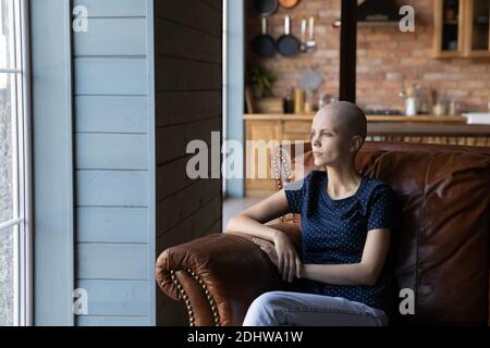 Nachdenkliche haarlose kranke Frau im Sessel sitzend, in der Ferne schauend Stockfoto