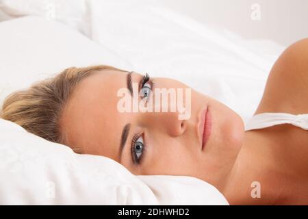 Eine junge blonde Frau liegt wach im Bett. Schlafflos und nachdenklich. Stockfoto