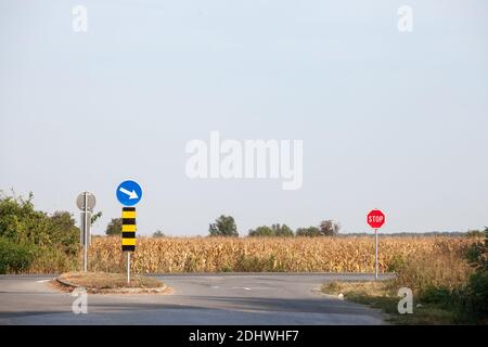 Europäische Kreuzung, eine Kreuzung zwischen zwei asphaltierten Straßen, mit Standard-Beschilderung und Stoppschilder, in einer ländlichen Umgebung. Bild eines typischen Stockfoto