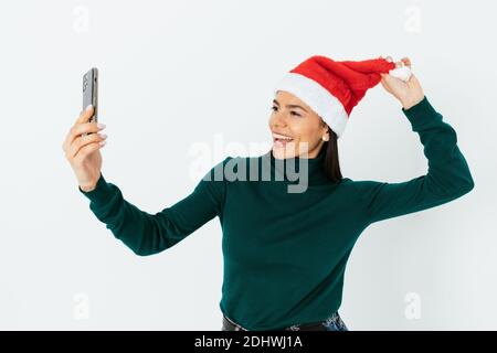 Attraktive junge Frau in santa Hut macht Selfie auf weiß Hintergrund Stockfoto