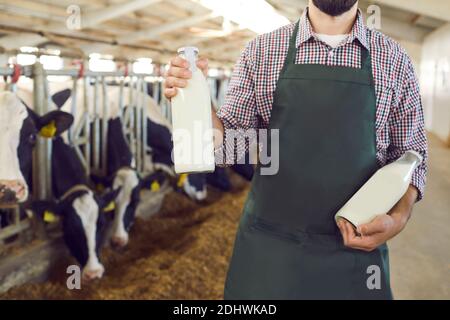 Zugeschnittenes Bild eines männlichen Bauern, der Glasflaschen mit frischer Bio-Milch auf einem Bauernhof hält. Stockfoto