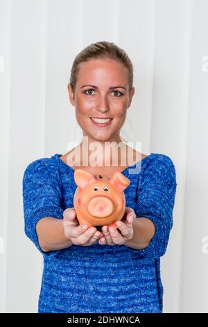 Eine junge Frau hält ein Sparschwein in ihrer Hand. Symbolfoto für Spare, Geld anlegen und Altersvorsorge. Stockfoto