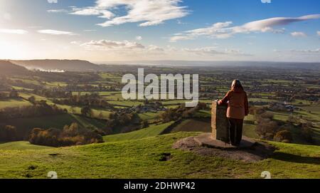 Frau, die die Aussicht vom Aussichtspunkt auf Coaley Peak, The Cotswolds, Gloucestershire, Großbritannien, bewundert Stockfoto