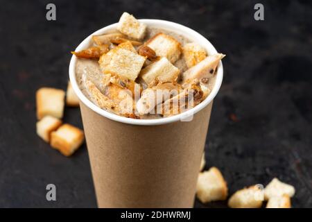 Französische Küche Lieferung von warmen Speisen - Nahaufnahme von Pilzsuppe mit Hühnerfleisch in Einweg-Pappbechern auf einer dunklen Steinoberfläche. Gesundes Lebensmittelkonzept, Stockfoto