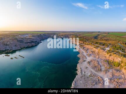 Alte geflutete Steinbruch mit großen Steinen am Abend warmes helles Licht mit kleinen trockenen Pflanzen in der malerischen Ukraine bedeckt. Luftpanoramik dro Stockfoto