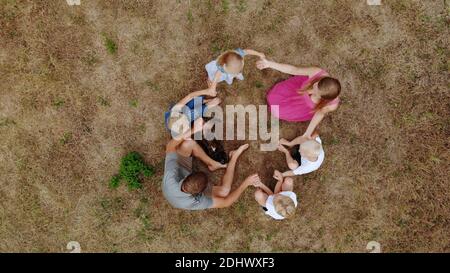 Freundliche Familie winkt mit den Händen, während sie mit einem Hund auf dem Gras sitzt. Blick von der Drohne. Stockfoto