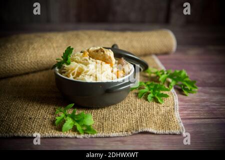 Leicht gekochter Reis mit Gemüse und Fleisch in einer Keramikschale auf einem Holztisch Stockfoto