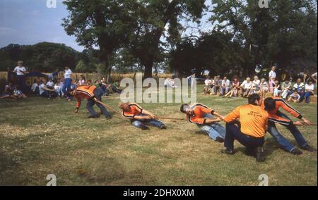 70er Jahre, historische, männliche Konkurrenten außerhalb des Feldes, die an einem Tauziehen des Krieges Contest, England, mit Trainer neben ihnen fordern mehr Aufwand. In einem Tauziehen-Ereignis müssen Mitglieder von zwei Mannschaften an einem Seil ziehen und es gegen die Kraft der Oppositionen zu ihnen bringen. Tauziehen hat eine lange Geschichte als Spaß-Aktivität bei Outdoor-Veranstaltungen und als Leistungssport, wie es war Teil des Olympischen Sommerprogramms in den Jahren 1900 bis 1920. Die British Tug of war Association wurde 1958 gegründet. Stockfoto