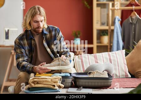 Junger Mann, der seine Kleidung in Koffer packt, geht er In den Urlaub Stockfoto