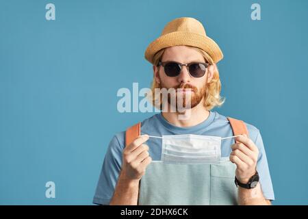 Porträt des Touristen in Sonnenbrille und Hut tragen schützende Maske auf blauem Hintergrund isoliert Stockfoto