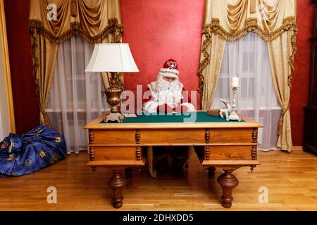 Der Weihnachtsmann schreibt eine Grußkarte, die am Tisch sitzt. Stockfoto