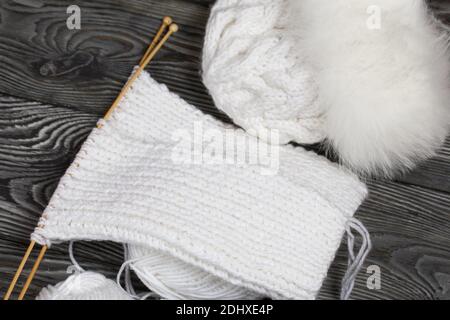Stricken mit Nadeln. Holzstricknadeln und weiße Fäden. Auf schwarzen Kiefernbrettern. Stockfoto