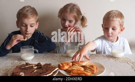 Mutter serviert Kekse auf dem Tisch und die Kinder essen es mit Milch. Stockfoto