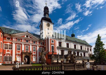 Broumov, Tschechische Republik - Juni 17 2020: Das Benediktinerkloster mit rot-weißer Fassade und die Kirche des hl. Adalbert aus dem 14. Jahrhundert. Sonniger Tag. Stockfoto