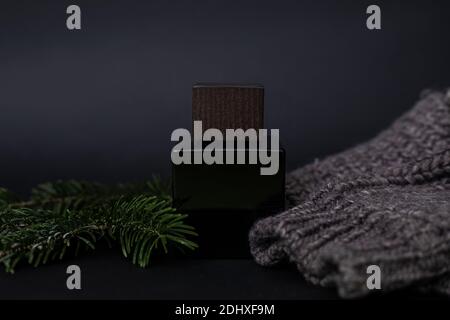 Parfüm, Herrenparfüm oder Lation nach der Rasur auf einem schwarzen neben einem Herrenpullover und Nadeln, Fichte. Luxus, Geschenk. Nahaufnahme Foto für Werbung ein Stockfoto