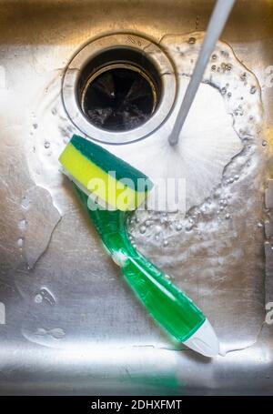 Wasser aus dem Wasserhahn läuft in Edelstahl Waschbecken mit Topf Schrubber liegt in ihm. Stockfoto