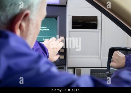 Grauhaariger Mann am Drive-up-Geldautomaten, der sich aus dem Autofenster lehnte und die Taste drückte - Anweisungen auf Englisch und Spanisch - Selektiver Fokus. Stockfoto