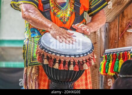 Mann im bunten Kostüm spielt afrikanische ethnische Percussion Trommel mit Quasten vor verschwommenem Hintergrund - abgeschnitten und Bewegungsunschärfe aktiviert Hände Stockfoto