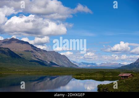 Farbenfrohe Sicht auf eine Holzhütte am spiegelglatten Round Tangle Lake, in dem sich ein Berg und der tiefblaue Himmel spiegeln. Stockfoto