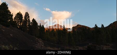 Spitze eines Vulkans zwischen sonnenbeschienenen Wolken mit einer Kiefer Wald unten Stockfoto