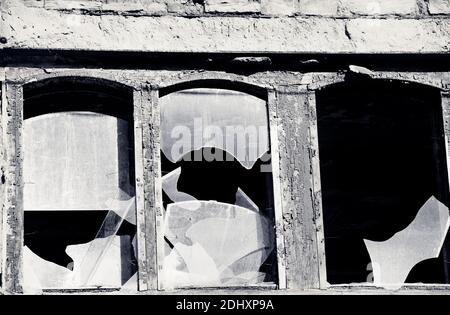 Die hölzerne Wand des alten zerstörten Hauses mit den zerbrochenen Fenstern. Schwarzweißbild. Hoher Kontrast. Stockfoto