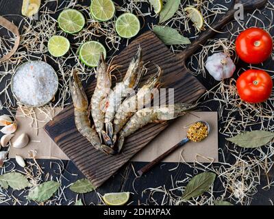 Frische Garnelen auf Küchentisch mit Zutaten. Rohe Garnelen, Tomaten, Salz, Limetten und Knoblauch Stockfoto