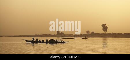 In Mopti, Mali, fahren die Menschen bei Sonnenuntergang mit dem Boot auf dem Niger, die sich vor dem glühenden Himmel in einer friedlichen westafrikanischen Szene abzeichnen. Stockfoto