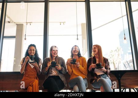 Vier stilvolle junge Frau mit Kaffee in einem Café sitzen. Gruppe von multiethnischen Freundinnen mit Kaffee und verbringen Zeit zusammen bei einem Kaffee sho Stockfoto