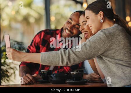 Eine Gruppe von Freunden, die Selfie im Café machen. Lächelnde Freunde treffen sich im Café und machen Selfie mit einem Handy. Stockfoto