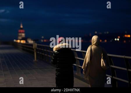 Istanbul, TUR. Dezember 2020. Zwei Frauen gehen an der Küste von Uskudar mit dem historischen Maiden-Turm im Hintergrund während einer Ausgangssperre am Wochenende, die zur Verhinderung der Ausbreitung der Coronavirus-Krankheit (COVID-19) in Istanbul, Türkei, verhängt wurde. Quelle: Jason Dean/ZUMA Wire/Alamy Live News Stockfoto