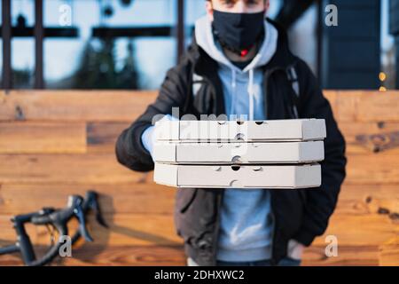 Der Lieferer hält Pizzataschachteln in einer ausgestreckten Hand. Lebensmittelzustellung, Fahrradkurier bei der Arbeit, Catering-Konzept zum Mitnehmen Stockfoto