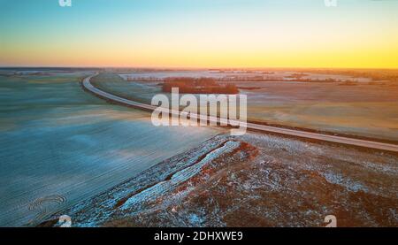 Winter grün Agrarfeld Winterpflanzen unter Schnee-Panorama. Highway Dezember Sonnenuntergang Luftaufnahme. Große Asphaltstraße. Blick auf die Landschaft von oben. Minsk Stockfoto