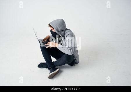 Ein Mann in einer Maske sitzt auf dem Boden innen Vor einem Laptop-Computer Hacking Verbrechen Stockfoto