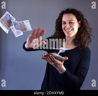 Lächelnde Frau mit lockigen Haaren wirft Banknoten in die Luft Stockfoto