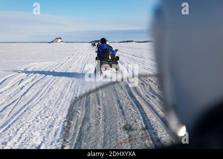 Inari, Lappland, Finnland - 2. März 2020: Schneemobil-Tour auf dem gefrorenen See von Inari, in Lappland, mit im Hintergrund Ukonkivi, einem heiligen Stockfoto