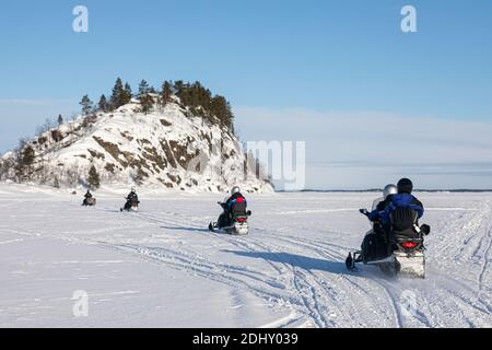 Inari, Lappland, Finnland - 2. März 2020: Schneemobil-Tour auf dem gefrorenen See von Inari, in Lappland, mit im Hintergrund Ukonkivi, einem heiligen Stockfoto