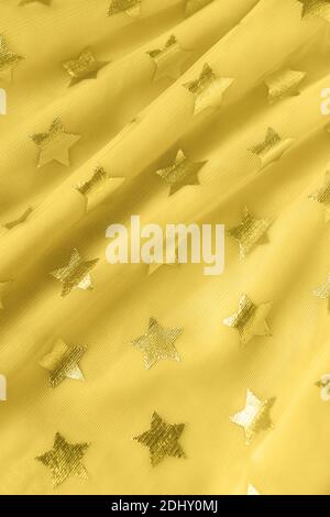 Hintergrund, Textur von leuchtend gelben Mesh-Gewebe mit Sternen. Konzept Trendfarbe des Jahres 2021 leuchtende, festliche Kleidung, feminin, Urlaub, bir Stockfoto