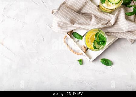 Sauges Wasser zur Entgiftung mit Zitrone, Gurke und Minze in Gläsern auf Holzschale auf weißem Beton-Hintergrund infundiert. Gesundes Lifestyle-Konzept. Top Vie Stockfoto