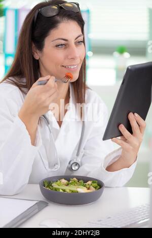 Schöne Geschäftsfrau ist mit gesunden Mittagessen während der Arbeit auf Tablet Stockfoto