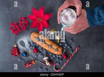 Weihnachtsfrühstück auf einem Steintisch Rollini mit Waldbeeren, einer Tasse Kakao und Marshmallow in den Händen eines Mannes in einem blauen Strickpullover, einem Pein Stockfoto