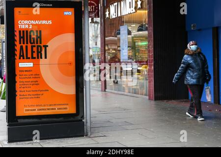 Eine Frau mit Gesichtsmaske kommt an einem digitalen Poster der COIVD-19-Informationskampagne vorbei, das in London ausgestellt wird. Stockfoto