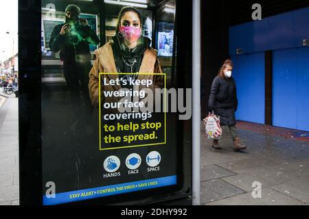 Eine Frau mit Gesichtsmaske kommt an einem digitalen Poster der COIVD-19-Informationskampagne vorbei, das in London ausgestellt wird. Stockfoto