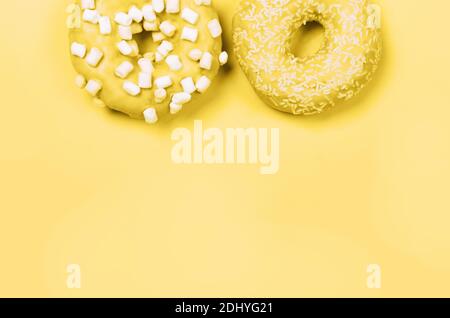 Farben des Jahres 2021. Grau und Gelb. Zwei Donuts mit Glasur auf pastellgelbem Hintergrund. Copyspace Stockfoto