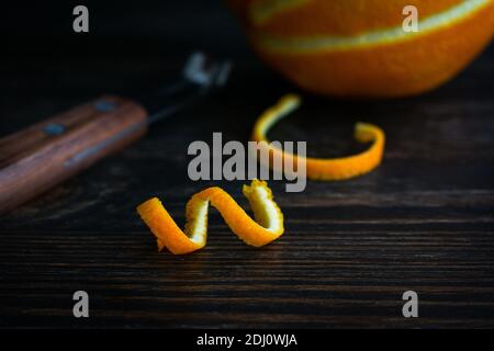 Orange Twist auf einem Sark Wood Hintergrund: Ein frischer Streifen Orangenschale und ein Kanalmesser Stockfoto