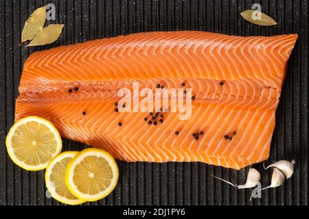 Rohes Lachsfilet auf dem Grillbrett mit Zitronenscheiben, schwarzen Pfefferkörnern, Knoblauch und Lorbeerblättern. Stockfoto