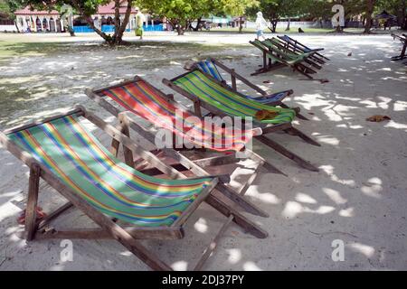 Hölzerne klappbare Chaiselongue stehen im Schatten der Bäume auf der Straße eines touristischen Resorts. Stockfoto