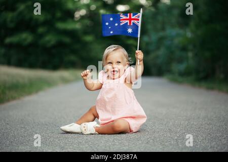 Niedlich liebenswert kaukasischen Baby Mädchen winkt australische Flagge. Lächelndes Kind, das auf der Straße im Park sitzt und den Australia Day feiert. Feiern Stockfoto
